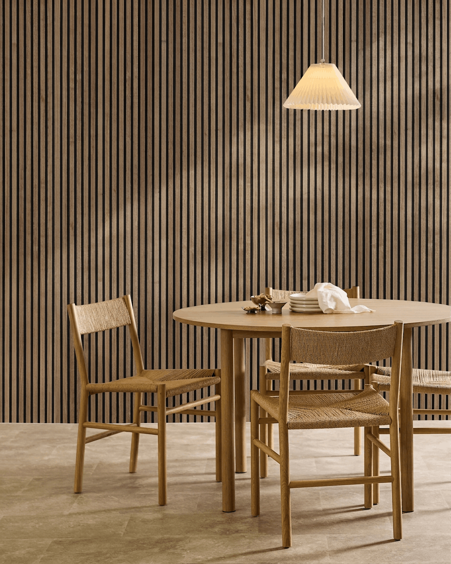 Minimalistische eethoek met een ronde tafel, gevlochten stoelen, hanglamp en een WoodUpp Akupanel akoestisch houten paneel in Natural Wood met black vilt aan de muur.